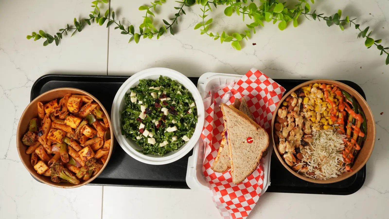 A day's five items laid out on a tray: a pasta bowl, a kale salad, a sandwich and a rice bowl.